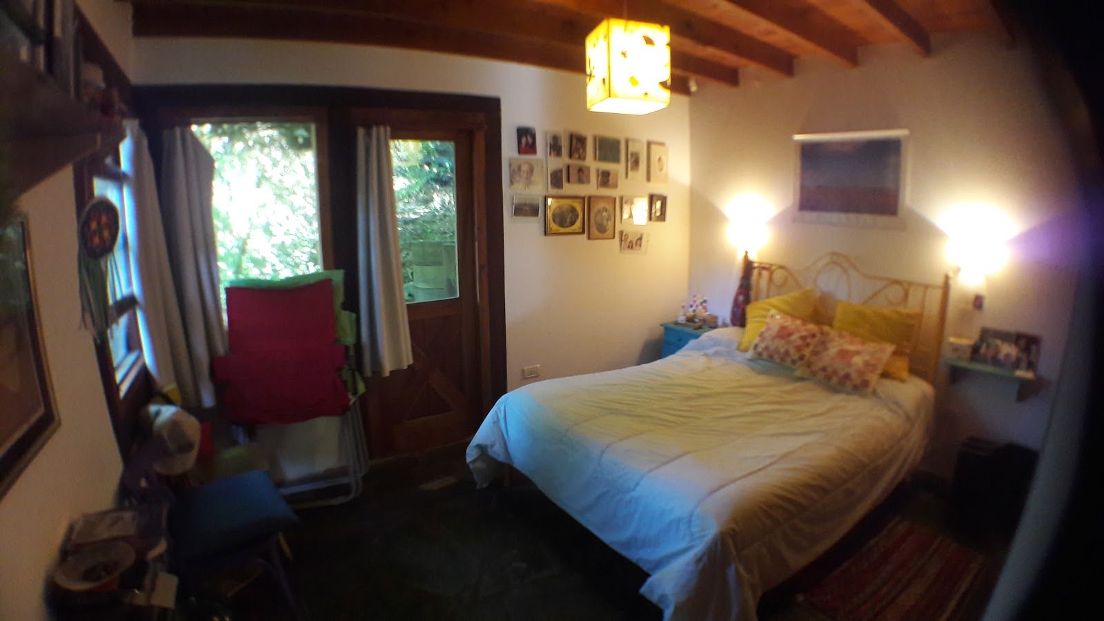 El dormitorio principal con cama matrimonial, veladores encendidos, vigas de madera a la vista y puerta vidriada al deck privado.