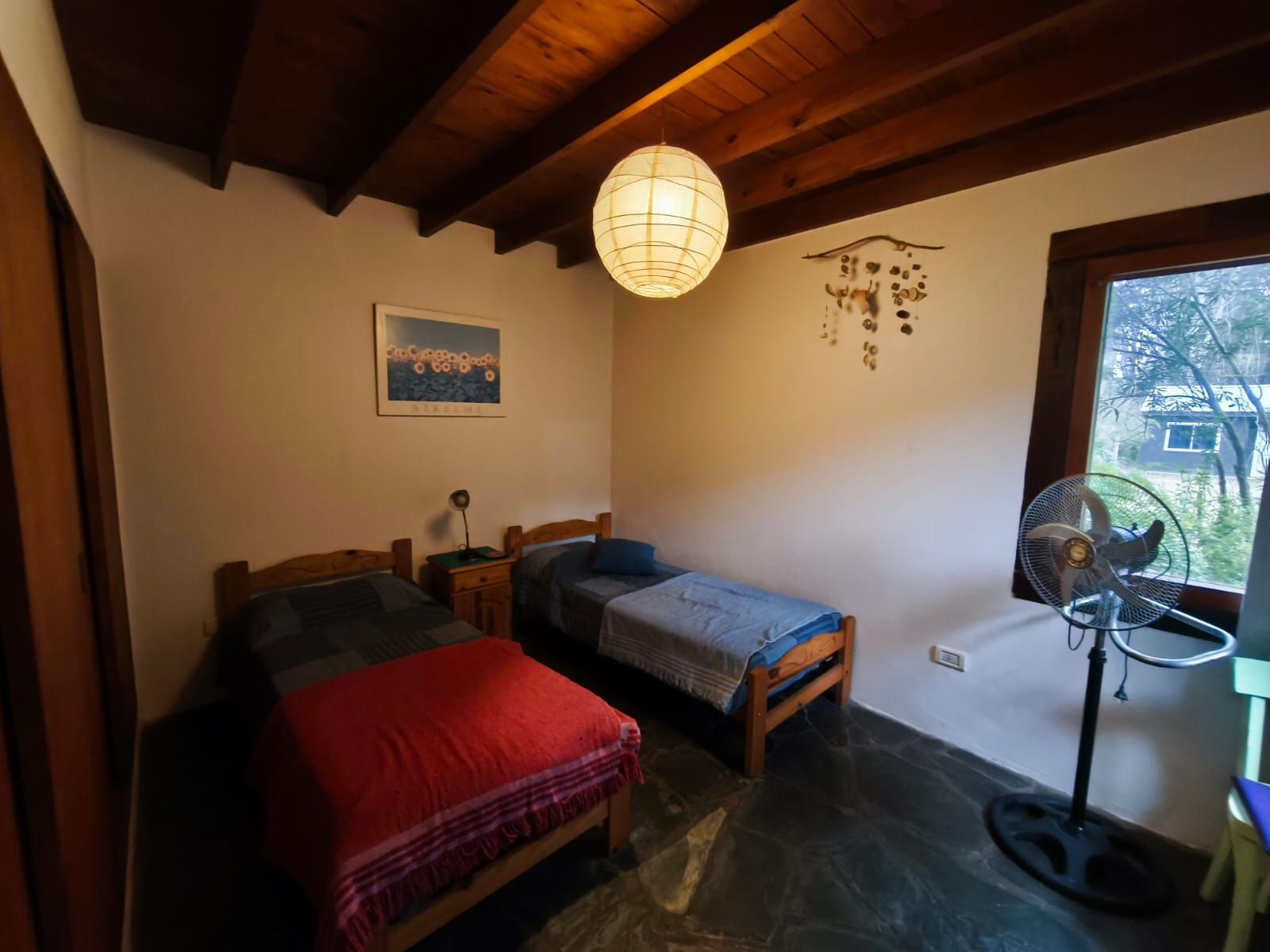 Segundo dormitorio con dos camas individuales, un móvil de caracoles colgando y la ventana al verde.