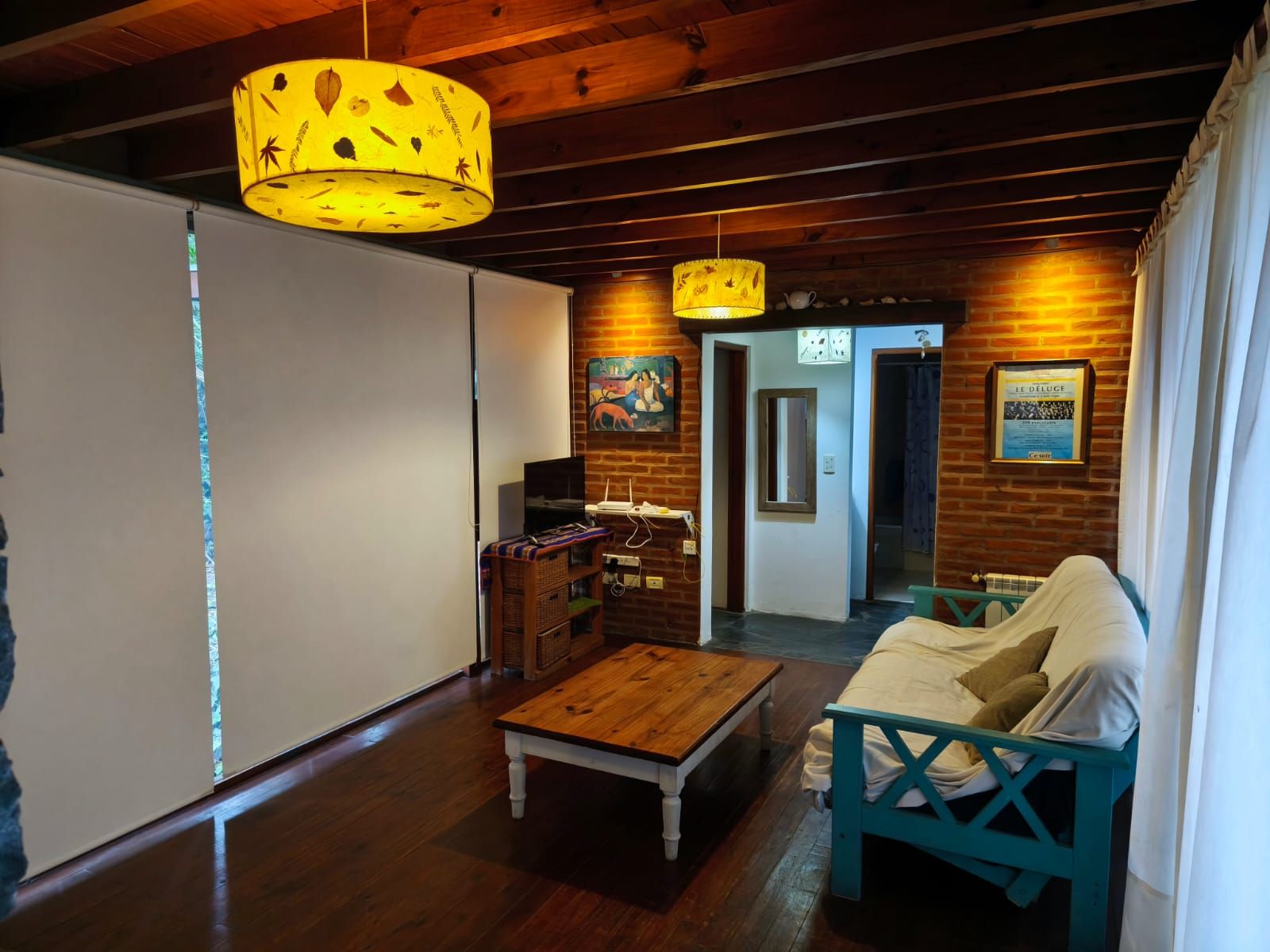 Rincón del living con futón turquesa, mesa ratona de madera y pared de ladrillo con cuadros, bajo la luz cálida de las lámparas.