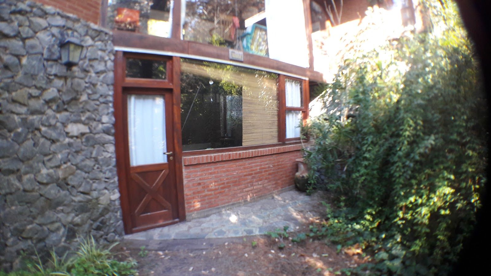El playroom vidriado de la planta baja visto desde el jardín, con puerta propia de madera, muro de piedra y zócalo de ladrillo.